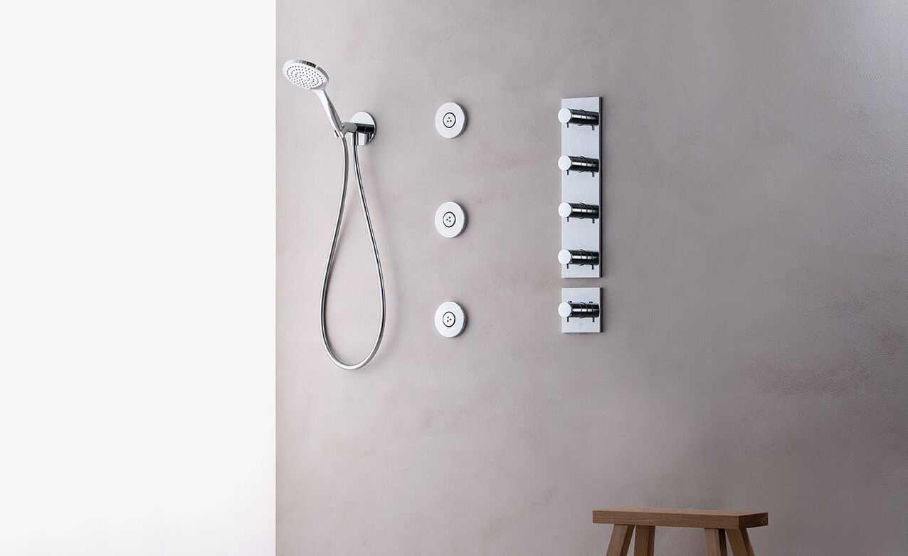 Minimalistische Dusche mit Wandbrause, Handbrause und mehreren Wasserdüsen. Schlichte graue Wände und ein Holzstuhl als Akzent. Minimalistische Dusche mit Wandbrause, Handbrause und mehreren Wasserdüsen. Schlichte graue Wände und ein Holzstuhl als Akzent.