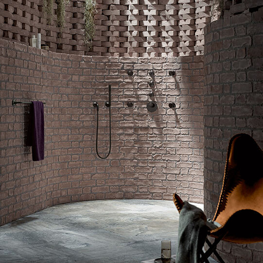 Rustikale Dusche mit freiliegenden Backsteinwänden in runder Form. Dunkle Armaturen und hängende Pflanzen. Gemütlicher Sessel und Bücherstapel als Dekor. Rustikale Dusche mit freiliegenden Backsteinwänden in runder Form. Dunkle Armaturen und hängende Pflanzen. Gemütlicher Sessel und Bücherstapel als Dekor.