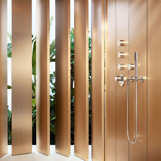 Luxuriöse Dusche mit goldenen Wänden und modernen Armaturen. Vertikale Lamellen bieten Sichtschutz, während Pflanzen im Hintergrund für einen natürlichen Akzent sorgen. Luxuriöse Dusche mit goldenen Wänden und modernen Armaturen. Vertikale Lamellen bieten Sichtschutz, während Pflanzen im Hintergrund für einen natürlichen Akzent sorgen.