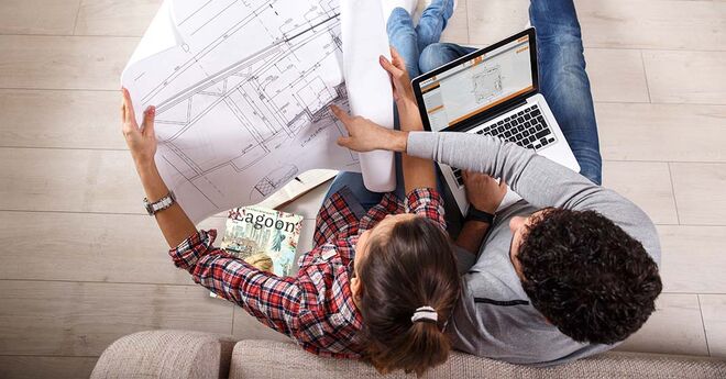 Zwei Personen sitzen auf einem Sofa. Eine Person hält einen Bauplan, während die andere auf einen Laptop schaut. Auf dem Tisch liegen Zeitschriften. Es wirkt wie eine Besprechung. Zwei Personen sitzen auf einem Sofa. Eine Person hält einen Bauplan, während die andere auf einen Laptop schaut. Auf dem Tisch liegen Zeitschriften. Es wirkt wie eine Besprechung.